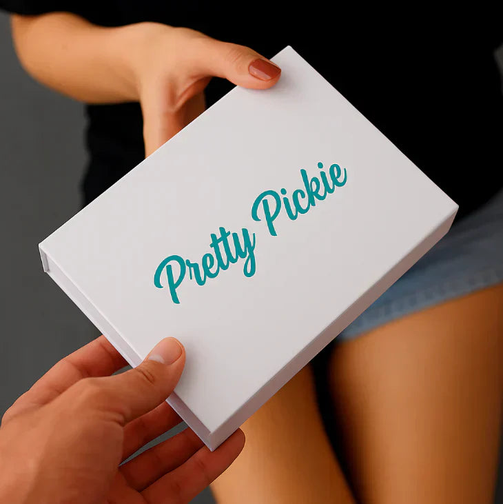 Hands exchanging a white Pretty Pickie box, symbolizing the DIY permanent jewelry kit, close-up with soft natural lighting and casual styling