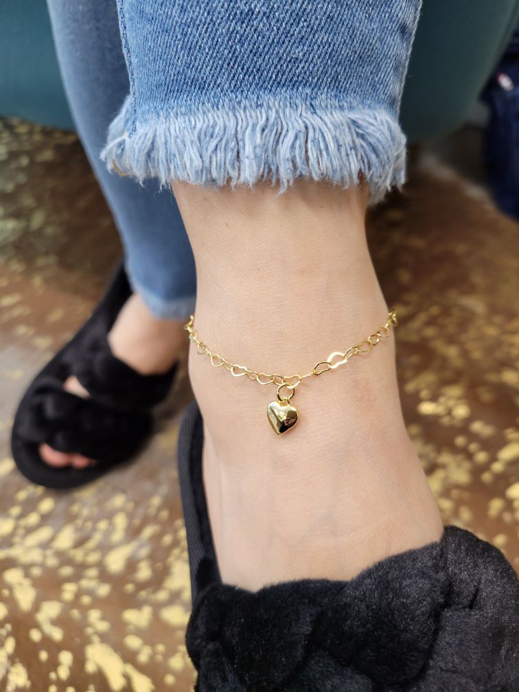 Close-up of a permanent ankle bracelet in gold, featuring a heart charm.