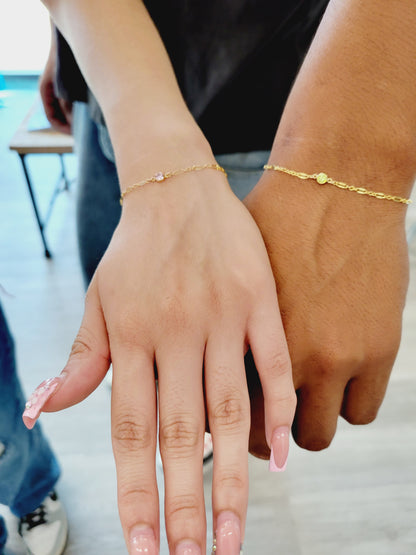 Two hands showing matching gold permanent bracelets with dainty birthstones, symbolizing friendship